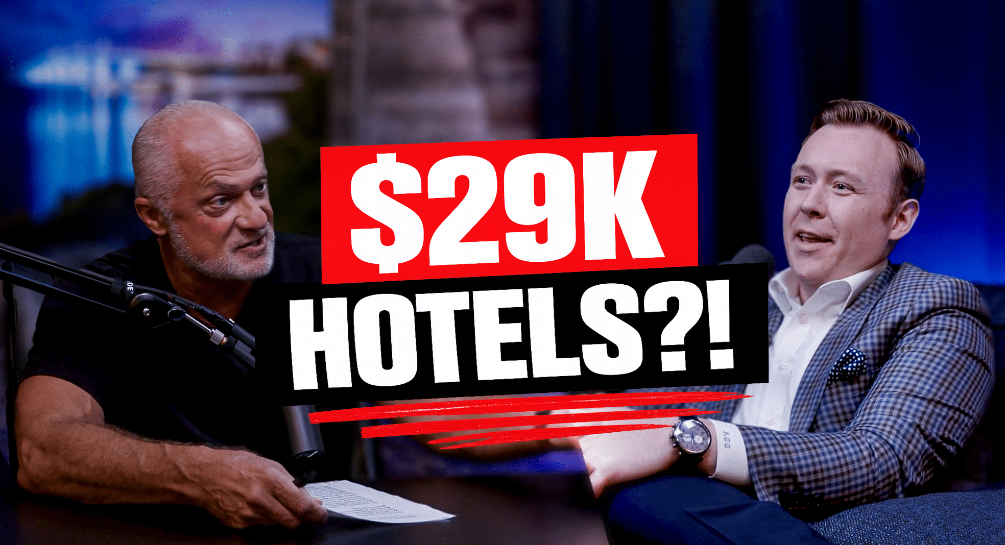 Two men sit at a studio table in a talk-show setting, with a bold red and white overlay displaying '$29K HOTELS?!' across the center.